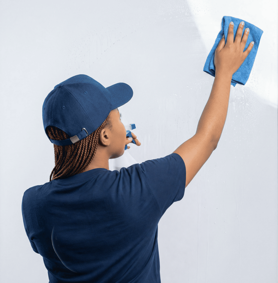 Blue Gloves Specialists cleaner in a navy cap and shirt wiping a glass surface with a blue microfibre cloth